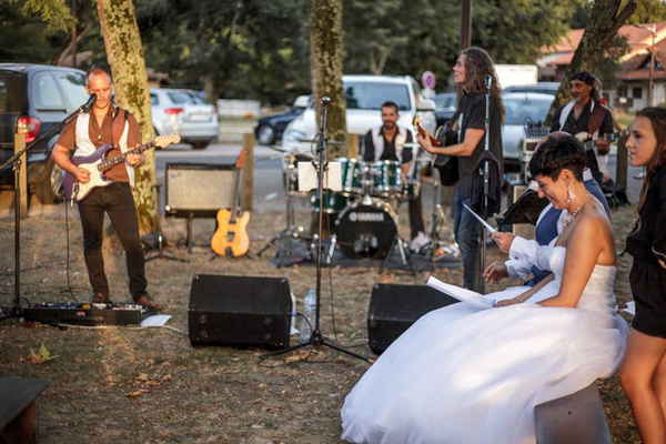 Bride and groom sitting down happily while listening to pop rock band in France perform at their outdoor wedding reception | Altus Entertainment