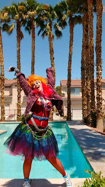 Cyndi Lauper impersonator posing with arms in air while standing in front of outdoor pool with palm trees | Altus Entertainment