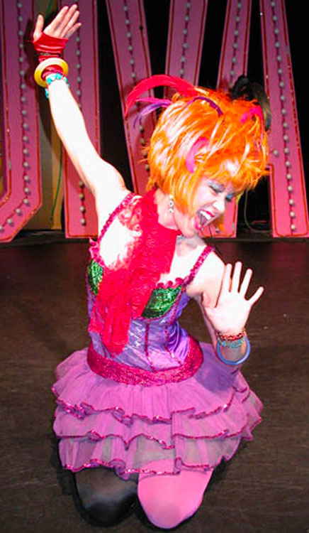 Female Cyndi Lauper impersonator kneeling on stage and reaching out happily while hands | Altus Entertainment