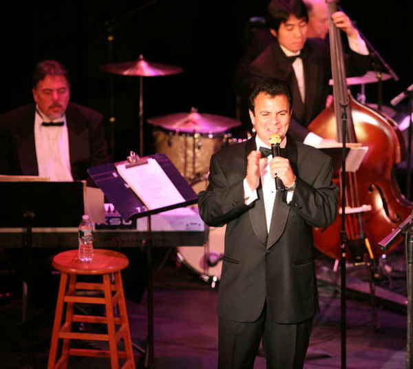 Male singer smiling to audience from stage while orchestra members perform alongside him | Altus Entertainment