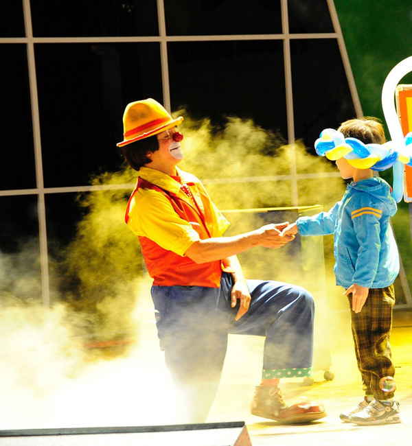 Professional picture of clown performer in Japan kneeling to boy and holding his hand during onstage show with fog pouring around them | Altus Entertainment