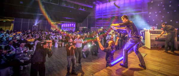 Wide angled picture of flair bartender pouring drink into glass sitting on another bartenders forehead and photographers take pictures | Altus Entertainment