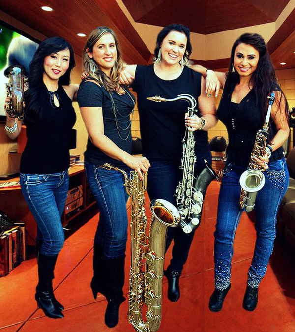 Four female musicians for yacht rock band for parties adorned in matching jeans and black shirts hugging one another and carrying instruments | Altus Entertainment