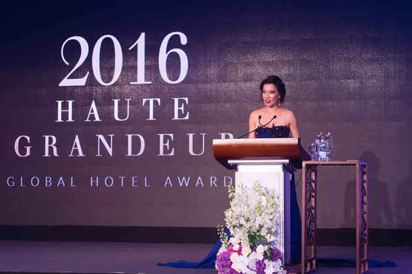 Female event emcee in Thailand standing at podium hosting 2016 global hotel awards ceremony | Altus Entertainment