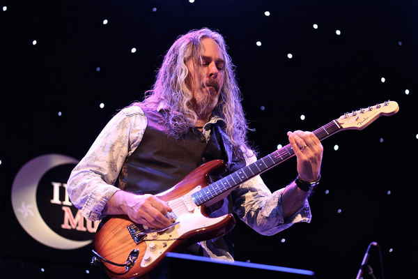 A man with long hair playing an electric guitar on stage as part of a Tribute Act. | Altus Entertainment